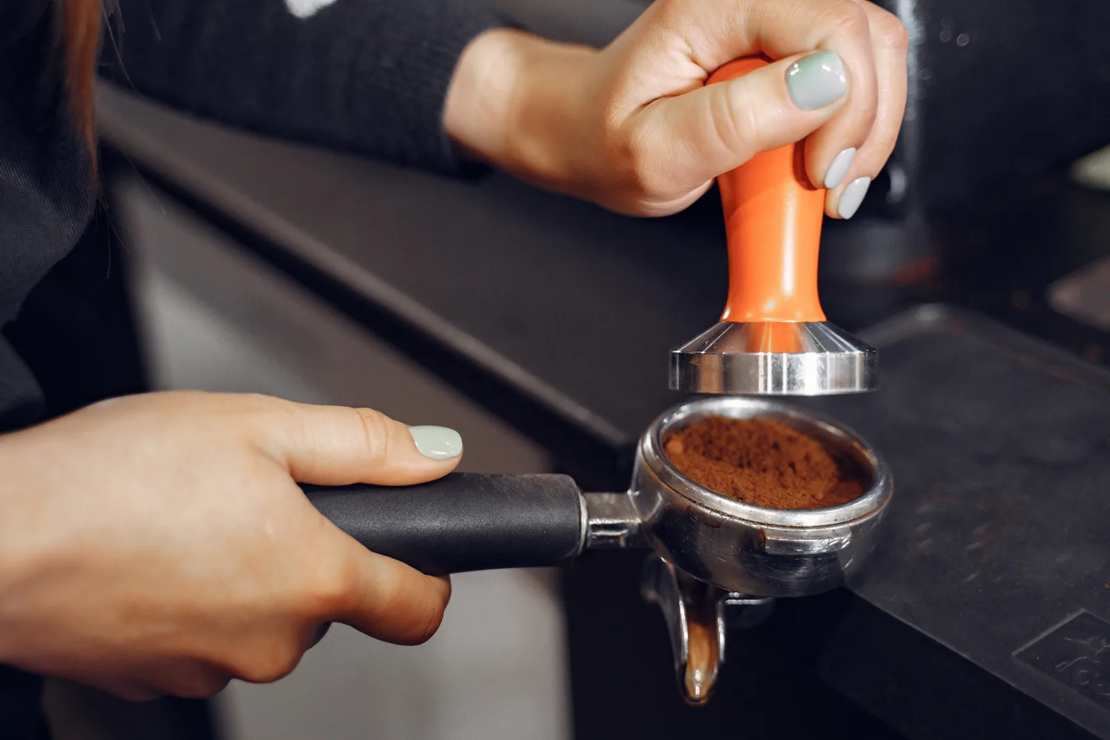 Hands tamping ground coffee with an orange tamper