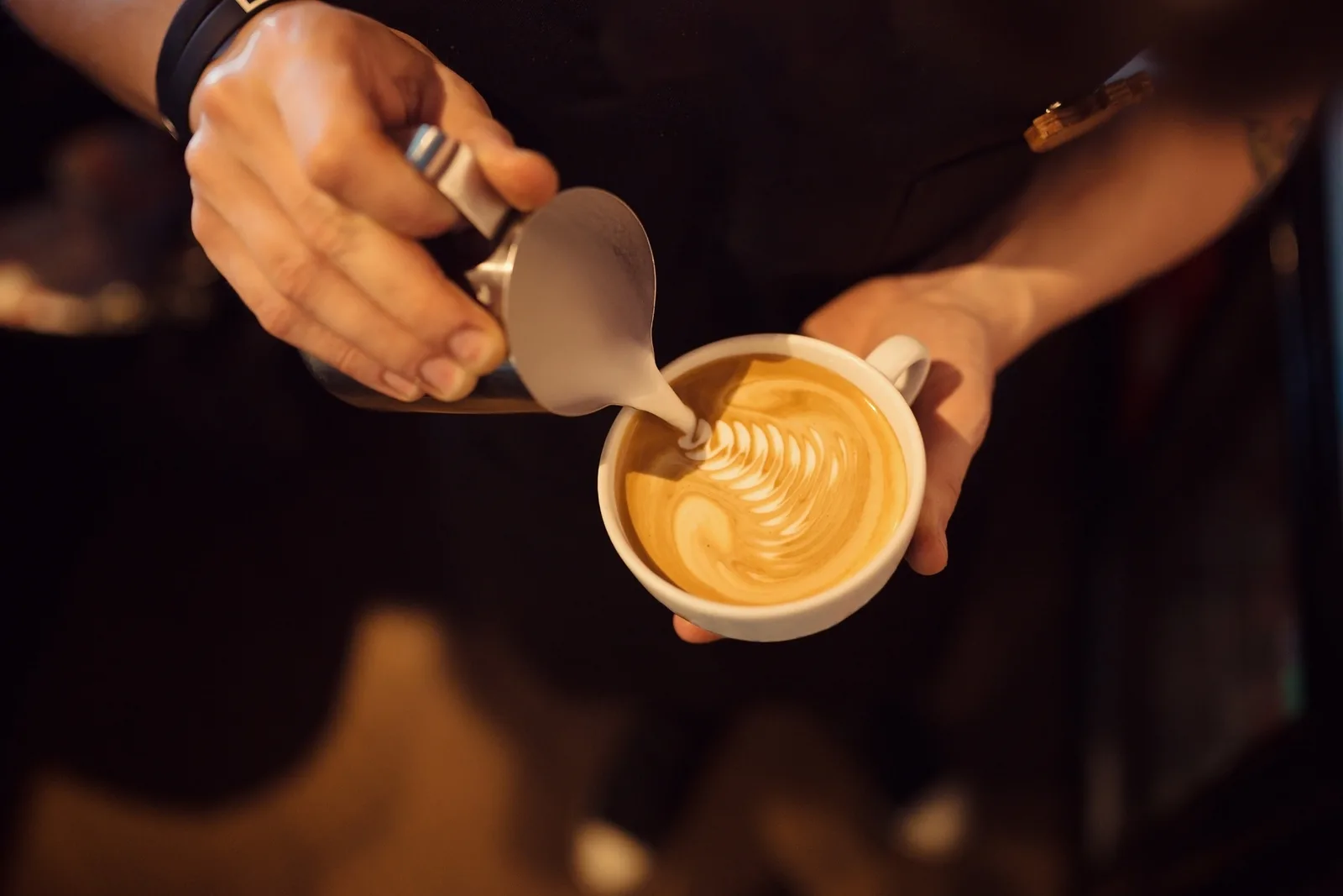 Hands pouring latte art into a cup