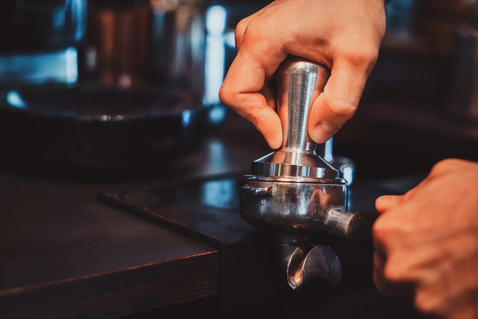 Hands tamping ground coffee into a portafilter