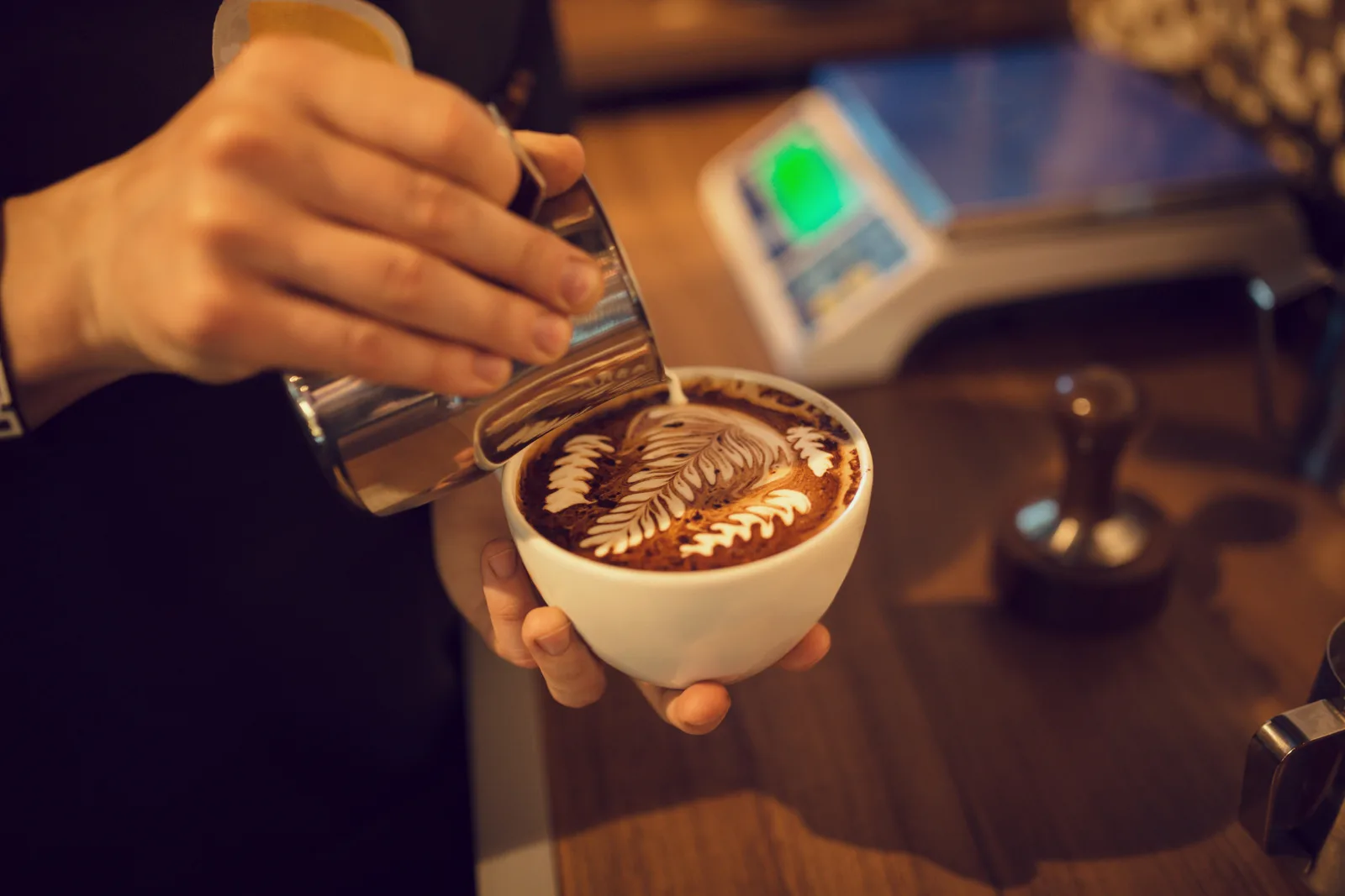 Hands pouring latte art into a cup